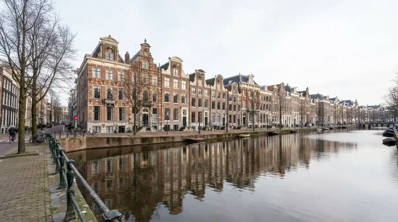 Een rij statige kantoorgebouwen staat langs een brede Nederlandse gracht onder een heldere lucht.